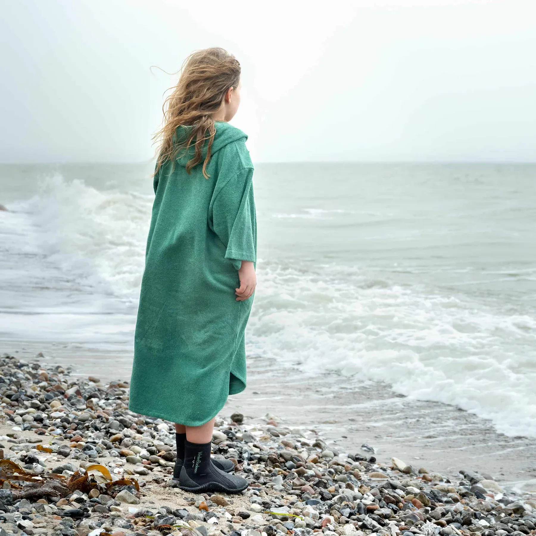 Barn iført turkis badeponcho Skagen på stranden efter badning
